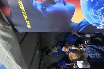 osoby pod namiotem pokazowym, po lewej roll-up z reklamą