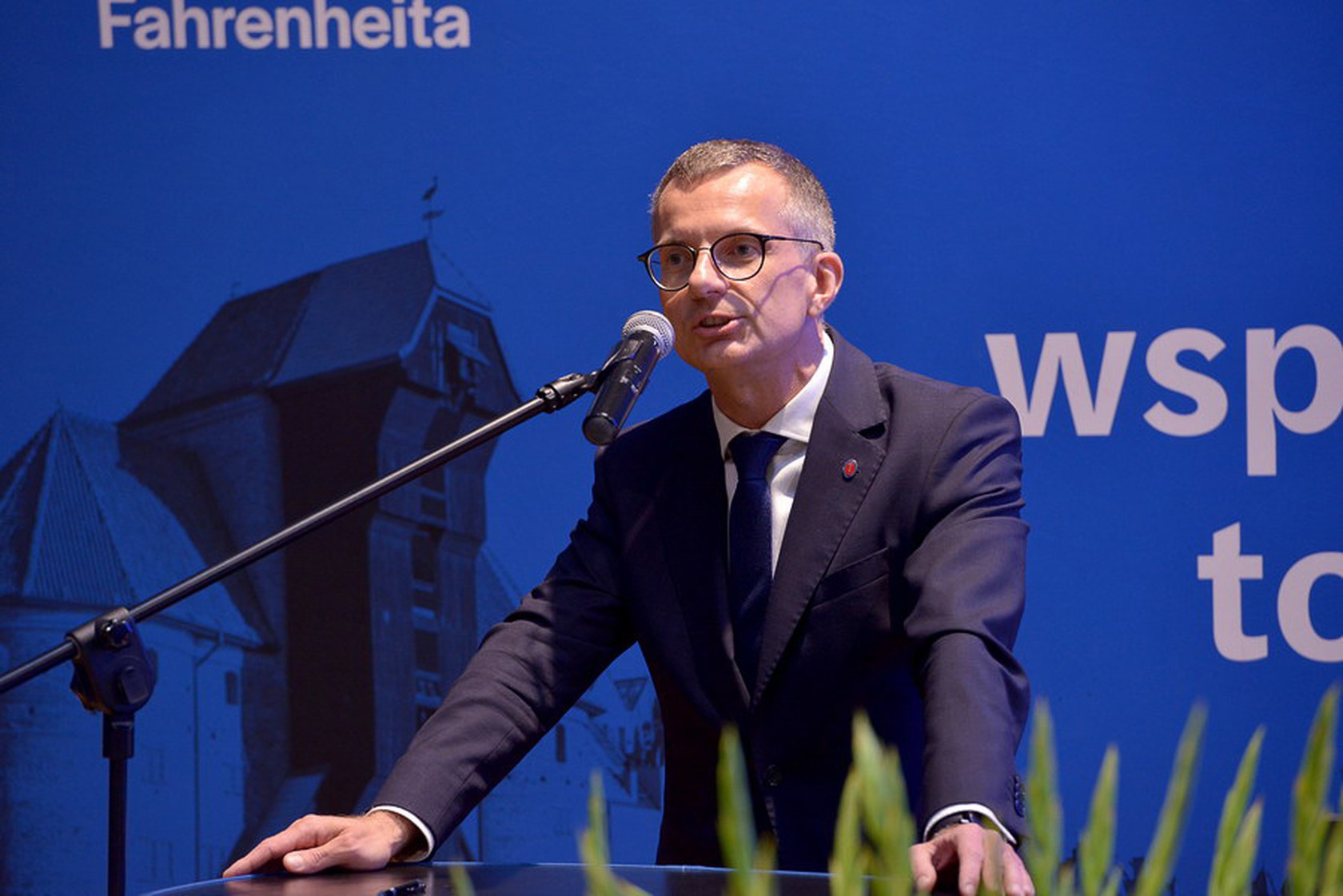 Mężczyzna w garniturze przy mównicy.