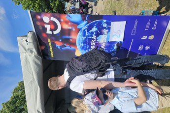 ludzie zaglądają do namiotu podczas pikniku, obok stoi roll-up Pomorskiej Nocy Naukowców