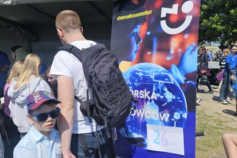 ludzie zaglądają do namiotu podczas pikniku, obok stoi roll-up Pomorskiej Nocy Naukowców