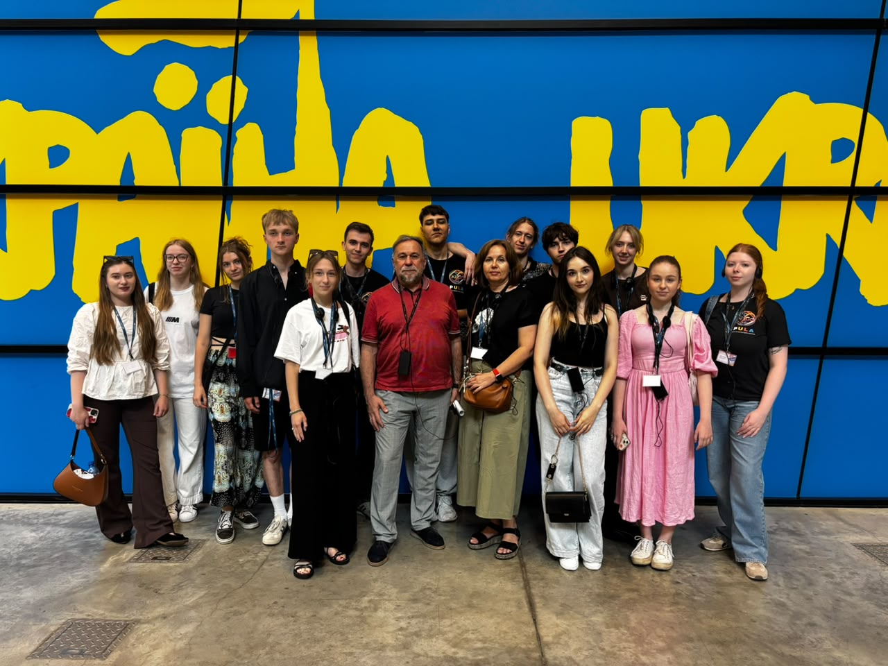 Photo of PULA project participants with their guide at the Solidarity Centre against the background of the famous "Ukraine" sign, modelled on the "Solidarity" sign designed by Jerzy Janiszewski.